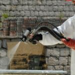 Green Insulation - a man in a white coverall spraying water on a brick wall