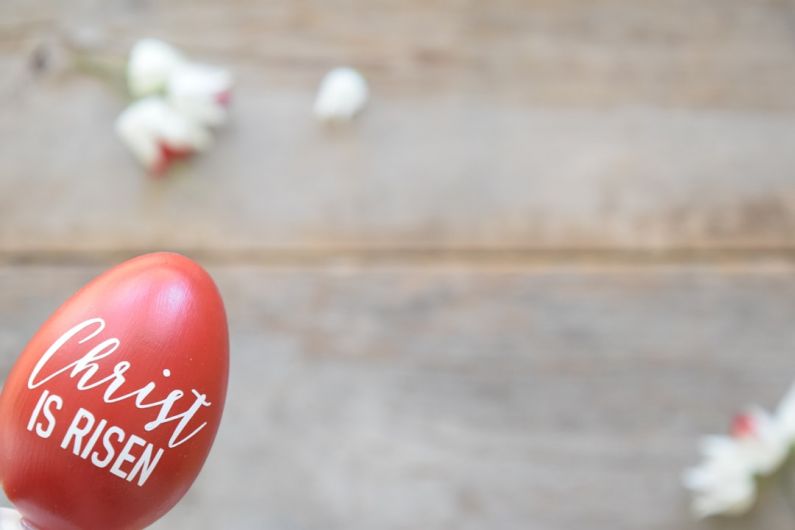 Easter Decor - a hand holding a red painted egg with the words cherry is risen written on it